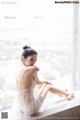 A woman sitting on a window sill in a white lingerie.