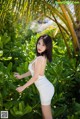 A woman in a white dress posing in front of a palm tree.