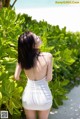 A woman in a white dress standing in front of a bush.