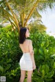 A woman in a white dress standing in front of a palm tree.