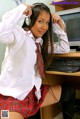 A woman in a school uniform sitting at a desk with headphones on.