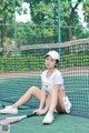 A woman sitting on a tennis court holding a racket.