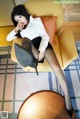 A woman sitting on a yellow chair wearing black stockings and high heels.