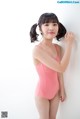 A young girl in a pink swimsuit leaning against a wall.