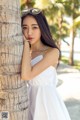 A woman in a white dress leaning against a palm tree.