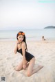 A woman in a black bathing suit sitting on a beach.