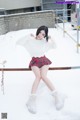 A woman in a white sweater and plaid skirt posing in the snow.