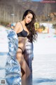 A woman in a black bikini standing in the snow.