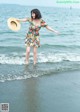 A woman in a floral dress and straw hat standing in the ocean.