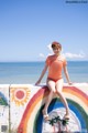 A woman in a bikini sitting on a wall by the ocean.