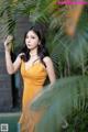 A woman in a yellow dress standing next to a palm tree.