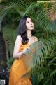 A woman in a yellow dress standing next to a palm tree.