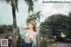 A woman standing next to a palm tree drinking from a bottle.