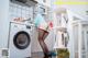 A woman in stockings and high heels standing in front of a washing machine.