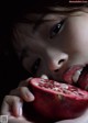 A young girl eating a pomegranate in the dark.