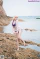 A woman in a bikini standing on a rock by the water.