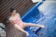 A woman in a pink bathing suit sitting on the edge of a swimming pool.