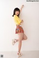 A woman in a yellow shirt and floral shorts posing for a picture.