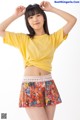 A young woman wearing a yellow shirt and a colorful skirt.