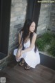 A woman in a white dress sitting on a wooden floor.