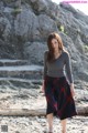 A woman standing on a rocky beach next to a rock.