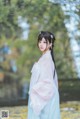 A woman in a blue and white hanbok standing in a park.