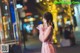 A woman in a pink dress standing on a city street at night.