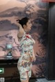 A woman in a cheongsam standing in front of a painting.