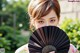 A woman holding a black fan in front of her face.