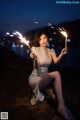 A woman sitting on a rock holding sparklers in her hands.