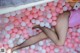 A woman laying in a ball pit filled with pink and white balloons.