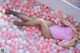 A woman laying in a bathtub filled with pink and white balloons.