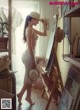 A naked woman standing in front of a painting on a easel.