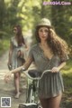 A woman in a dress and hat standing next to a bike.