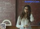 A woman wearing glasses standing in front of a blackboard.