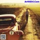 A man walking down a dirt road next to a red car.