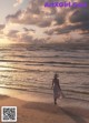 A woman in a white dress and hat walking on the beach.