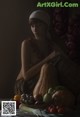 A naked woman sitting in front of a pile of vegetables.