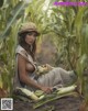 A woman in a straw hat sitting in a corn field.