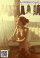 A naked woman standing in front of a window next to a bunch of underwear.