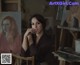 A woman sitting in front of a painting on a easel.