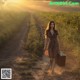 A woman walking down a dirt road carrying a suitcase.