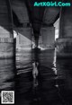 A naked woman standing in the water under a bridge.