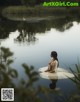 A woman sitting in the water with a swan in the background.