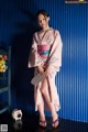 A woman in a pink kimono standing in front of a blue wall.