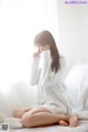 A woman sitting on a bed in a white shirt.