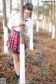 A young woman in a school uniform leaning against a tree.