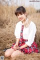 A young woman in a school uniform sitting in a field.