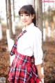 A woman in a school uniform leaning against a tree.