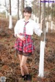 A woman in a school uniform leaning against a tree.